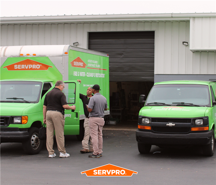 two green servpro of northwest orlando box trucks, 3 servpro employees standing by one with the door open, front of warehouse